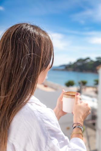 a woman holding a cup of coffee near the beach at La Muntanya in Llafranc