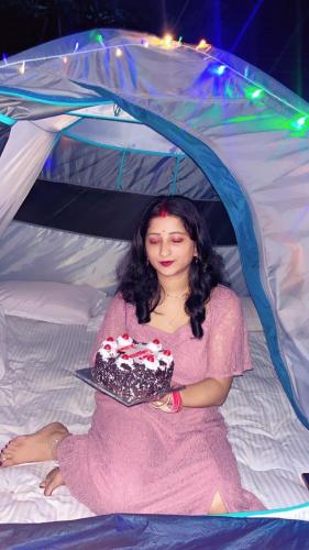 a woman sitting on a bed holding a cake at TEC Resort and bar in Dharān Bāzār