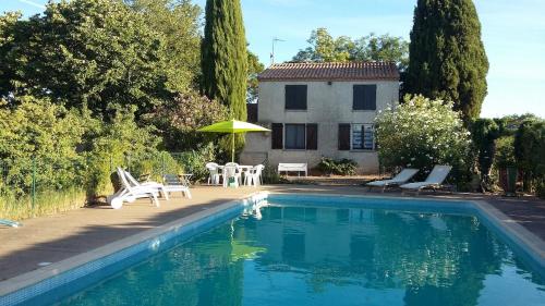 une piscine avec des chaises et un parasol ainsi qu'une maison dans l'établissement Gite Saint Irénée, à Béziers