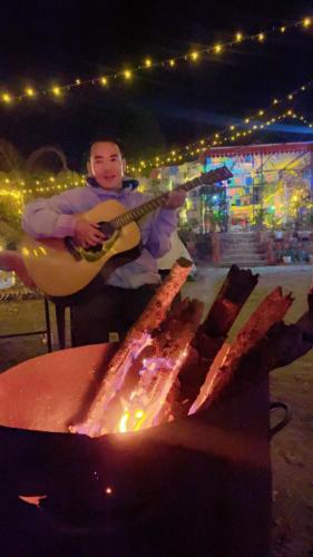 a man playing a guitar in front of a fire at TEC Resort and bar in Dharān Bāzār