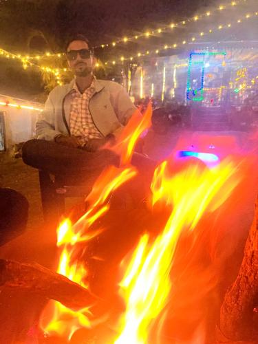 a man sitting next to a bonfire at night at TEC Resort and bar in Dharān Bāzār