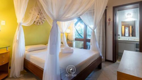 una camera con letto a baldacchino e tende bianche di Casa na Praia de Mucugê - Arraial D'ajuda - Bahia - 40m da praia - Ar condicionado - vaga de estacionamento - Wifi a Arraial d'Ajuda