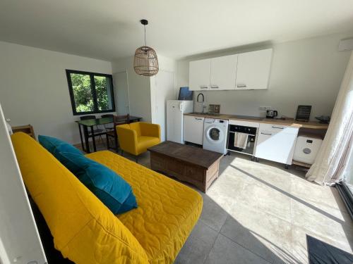 un salon avec un canapé jaune et une cuisine dans l'établissement Petit gîte cosy proche de la mer, jardin privatif, à Clohars-Fouesnant