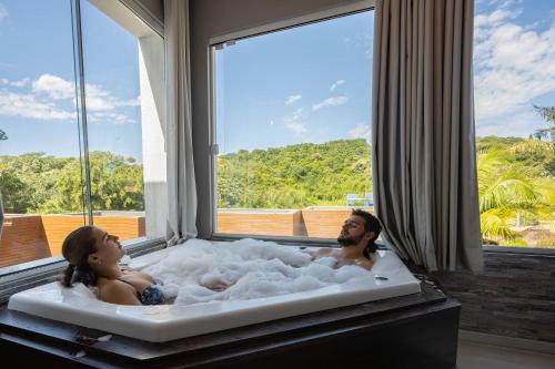 a man and a woman in a bath tub with a window at Pousada Natribus Rosa in Praia do Rosa