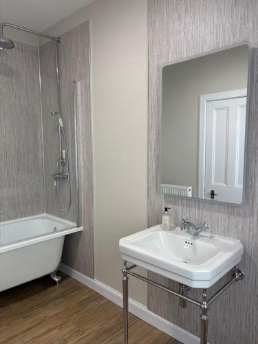 a bathroom with a sink and a tub and a mirror at Drumlinn Cottage in Bridge of Cally