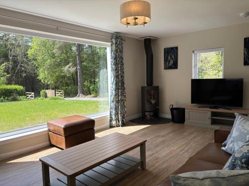 a living room with a large window and a tv at Drumlinn Cottage in Bridge of Cally