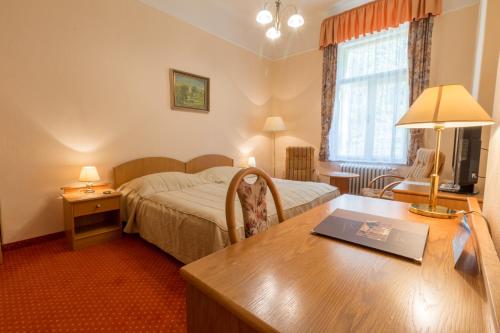 a hotel room with a bed and a desk with a table at Ensana Svoboda in Mariánské Lázně