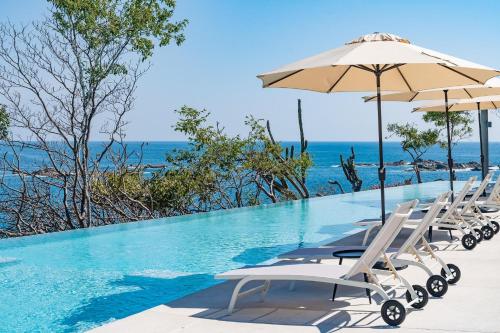 a pool with chairs and an umbrella and the ocean at 3061 - Amanecer B2 in Tangolunda
