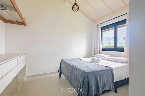 a white bedroom with a bed and a window at Apto em Cond. c/piscina em Praia do Forte CVAF0220 in Praia do Forte
