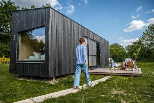 a boy standing in front of a black tiny house at Twente Cabin Tilligte in Tilligte