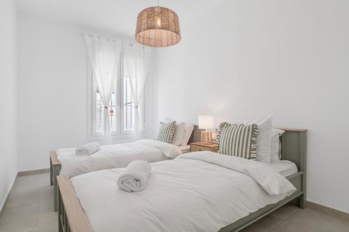 two beds in a white bedroom with a chandelier at La Casa de Emilie in Conil de la Frontera
