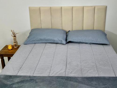 a bed with two blue pillows and a table at Apto Vida Boa 2 - 250m do mar in Palhoça