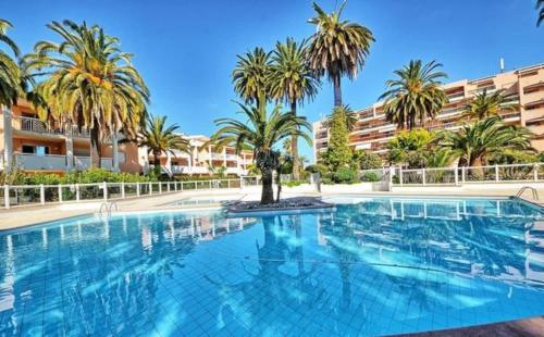 une grande piscine avec des palmiers en face d'un bâtiment dans l'établissement Appartement 2 chambres à 5 min à pieds de la plage et tout commerce, à Vallauris