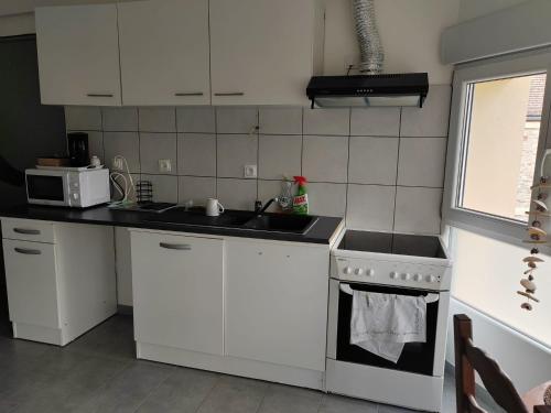 une cuisine avec des armoires blanches, un évier et une cuisinière dans l'établissement Agréable studio près de cergy, à Ableiges