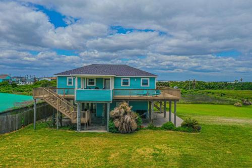 a blue house with a deck on a grass field at Fly Away to Sea Bird Life is Better in Flip-Flops in Galveston