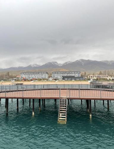 a pier in the water with buildings in the background at Issyk Kul in Korumdy