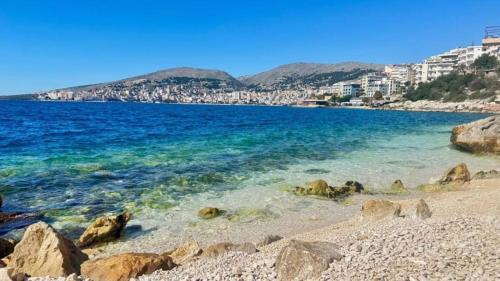 a beach with rocks and the water and buildings at War Bunker Hostel in Sarandë