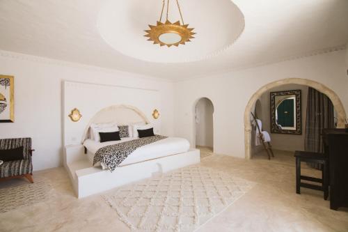 a white bedroom with a bed and a chandelier at Dar Naël in Houmt Souk
