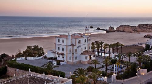 a white building on the beach next to the ocean at Bela Vista Hotel & Spa - Relais & Chateaux in Portimão