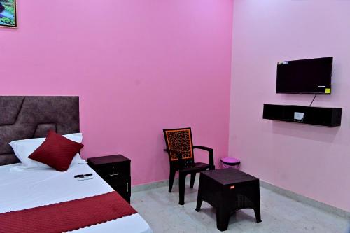 een slaapkamer met een roze muur met een bed en een stoel bij The Sunrise Ayodhya Guest House in Ayodhya