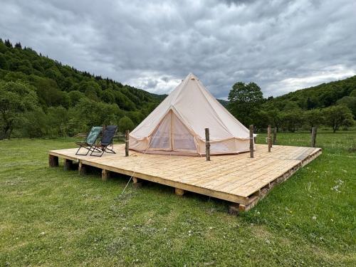 una tienda de campaña y dos sillas en una terraza de madera en Glamping - Casuta de pe Fiad, en Romuli