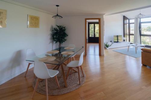 a dining room with a glass table and white chairs at ÁTICO CON VISTAS Centro Histórico in Allariz