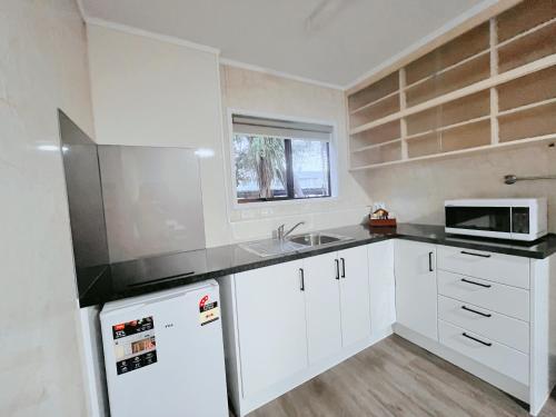 a kitchen with white cabinets and a sink and a microwave at Beetham Park Motel in Hamilton