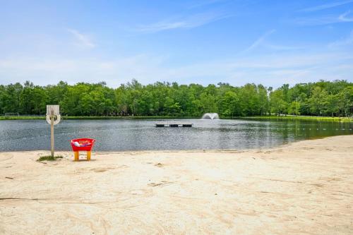 a red chair sitting on a sandy beach next to a lake at Atlas Point Lodge Sauna Fireplaces Kayaks Lakes Pet-Friendly Yard in Pocono Lake