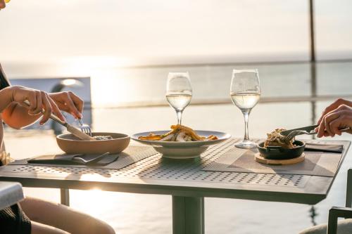 two people eating food on a table with glasses of wine at Serenità Luxury Suites in Akrotiri