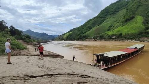 a man and a woman standing next to a boat on a river at 2 days Mekong cruise package with Mekong Lover Cruise from Houay Xay to Luang Prabang or Mekong cruise from Luang Prabang to Huay Xai - Thailand in Ban Khonkèo