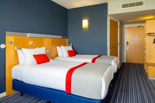 two beds in a hotel room with red and white pillows at Holiday Inn Express London - Epsom Downs by IHG in Epsom