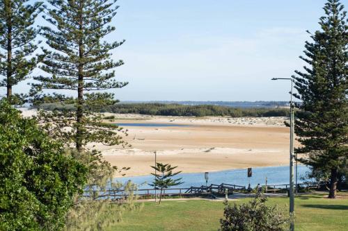 a view of a beach with trees in the foreground at Caprina at Happy Valley - Beachfront Escape in Caloundra