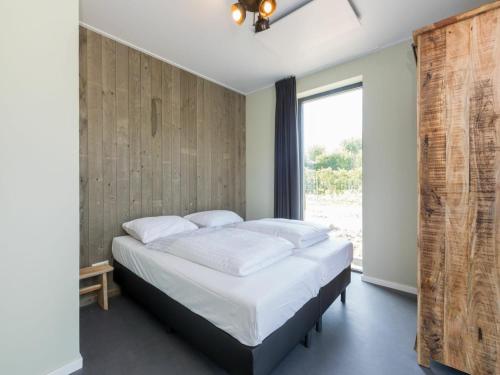 Un dormitorio con una cama con sábanas blancas y una ventana. en Holiday Home in Vrouwenpolder near Beach, en Vrouwenpolder
