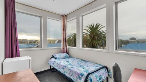a room with windows and a bed and a table at Christchurch Backpackers and Cafe in Christchurch