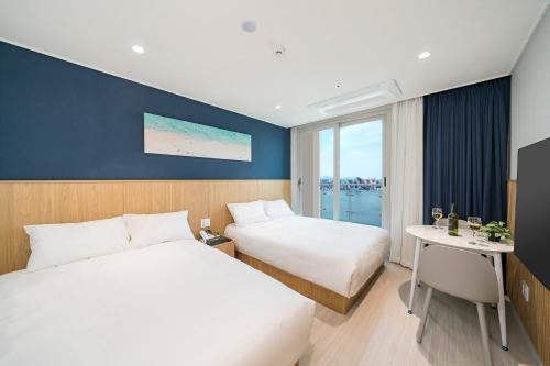 a hotel room with two beds and a desk and a window at Sokcho Mari Vista Hotel in Sokcho