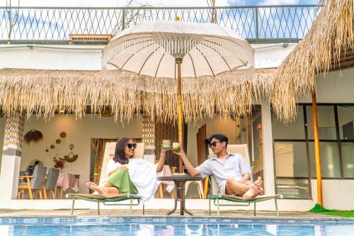 two people sitting in chairs under an umbrella next to a pool at D'svarga Glamping in Seturan