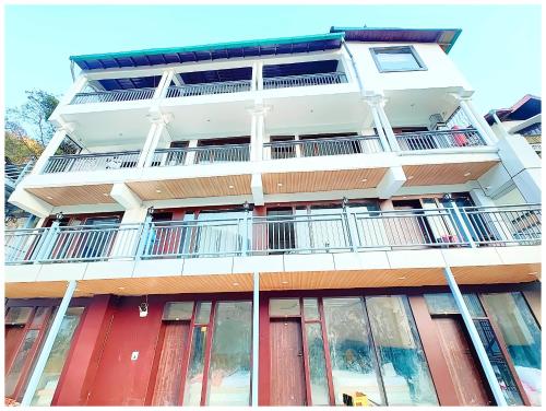 a tall white building with red doors and windows at NAINITAL HOTEL A LUXURIOUS RESORT'S PRANAV! INN - Free Parking & Wi-fi - Restaurant & Room Service - Spacious & Comfortable Rooms With Hill View Available -Near Bhowali Road - Best Hotel In Nainital in Bhowāli