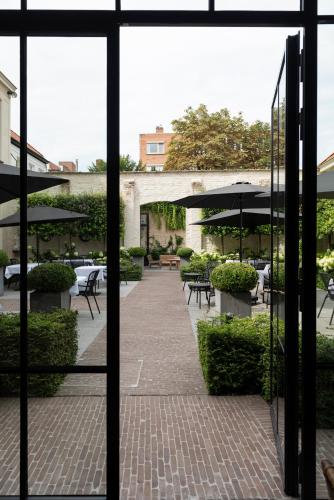 a view through a window of a patio with tables and umbrellas at Cobergher Hotel in Kortrijk