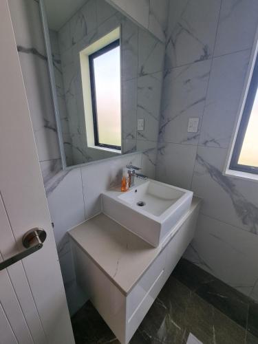 a white bathroom with a sink and a mirror at BEHOME - Modern Guest Suite in Kumeu