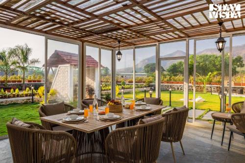 a dining room with a table and chairs and windows at StayVista at The Five Oaks - Private Pool Cottages in Karjat