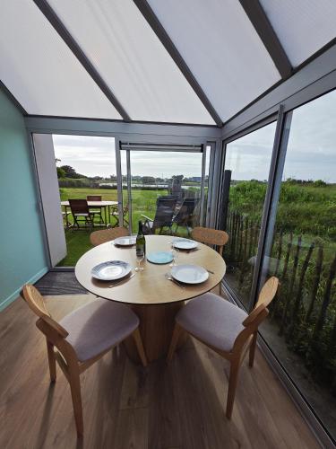 une salle à manger avec une table, des chaises et des fenêtres dans l'établissement Charmante maison avec vue mer panoramique et acces direct aux magnifiques plages, à Plouguerneau