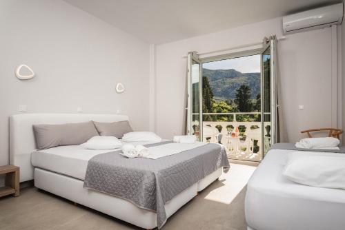 a white bedroom with two beds and a large window at Kokkari Beach Hotel in Kokkari