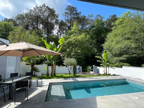 a swimming pool with a table and an umbrella at Spacious Luxury Modern Villa with Pool, Beaches and Garden in Saint-Martin-de-Seignanx