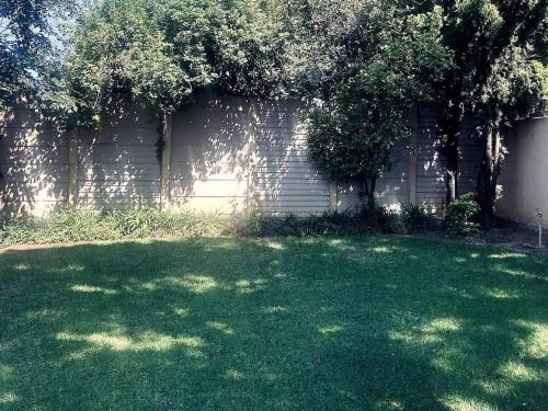 a green yard with trees and a brick wall at Tranquility Guesthouse JHB in Kempton Park