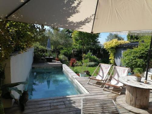 - une piscine avec 2 chaises, une table et un parasol dans l'établissement Maison Bohème, à Verfeil