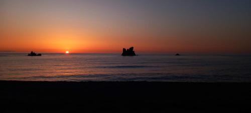 a sunset on the beach with people in the water at Sa Mesaluna Naturhouse in Ilbono