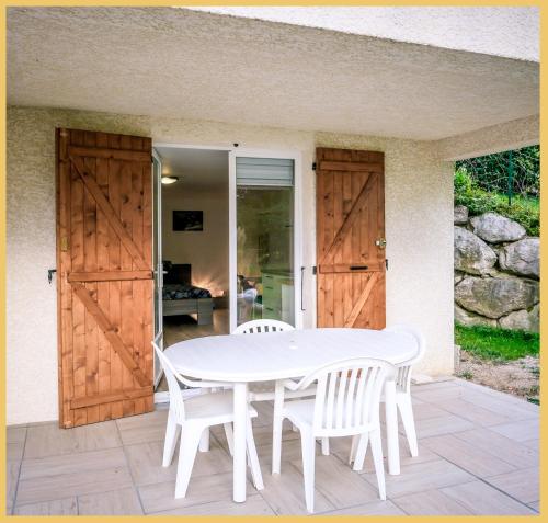 une table blanche et des chaises sur un patio avec des portes en bois dans l'établissement Chez Bert I Studio I Perrignier, à Perrignier