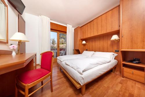 a bedroom with a bed and a desk and a red chair at Beach Hotel Rosa in Malcesine
