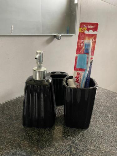 a black bottle of soap and a toothbrush holder on a counter at Scenic Cozy Retreat in Islamabad in Islamabad