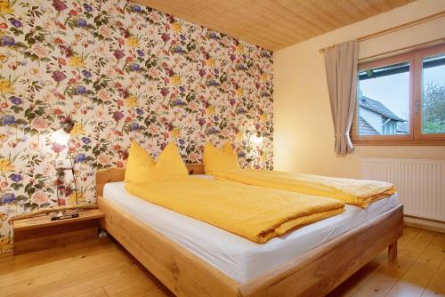 a bedroom with a bed with yellow sheets and floral wallpaper at Ferienhaus am Ried in Burgweiler